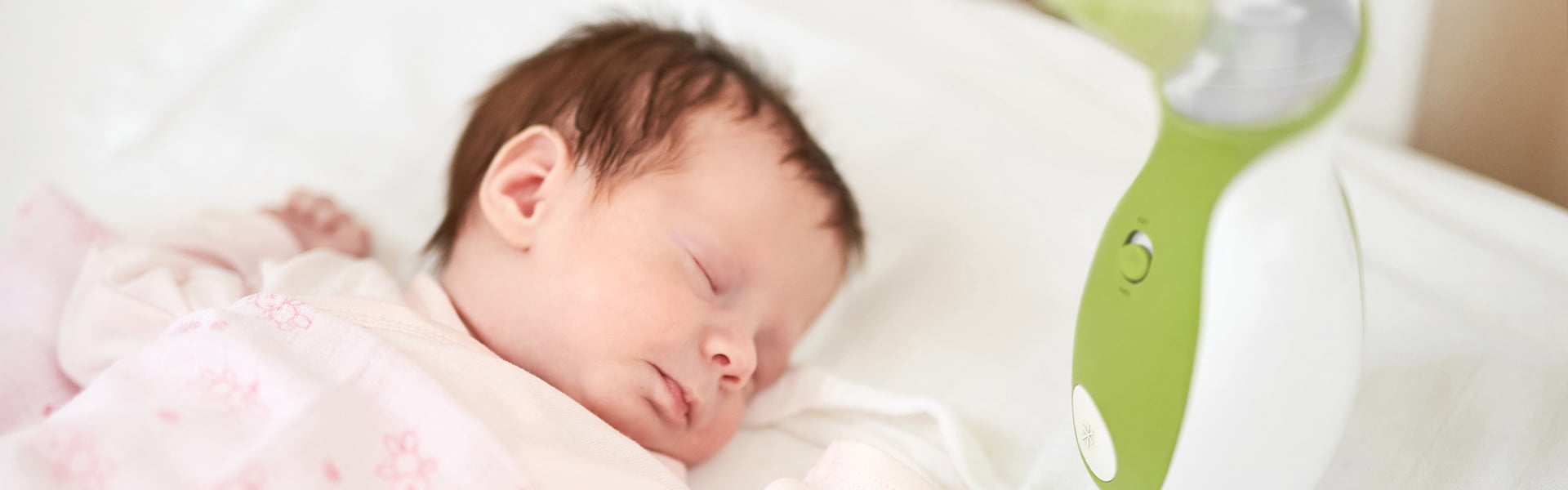 A baby sleeping peacefully in the baby cot bed next to the Nosiboo Go Portable Nasal Aspirator