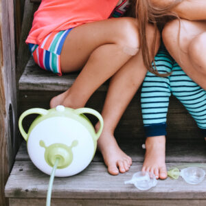 A Nosiboo Pro electric nasal aspirator with a disassembled Colibri head on the stairs next to two little girls.